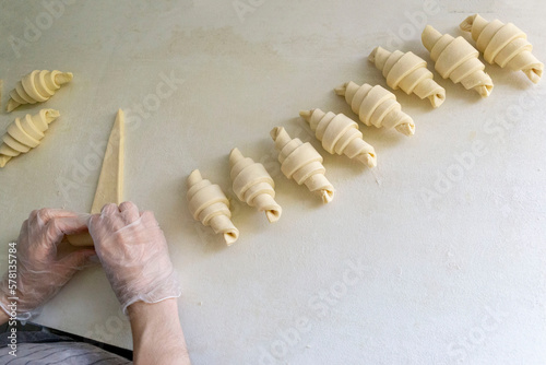 Baker in gloves rolling the dough into a croissant on the table one by one