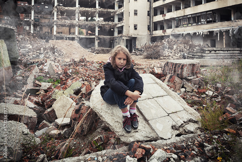 little girl sitting among ruins of house. Refugees concept. War crisis in Ukraine. Humanitarian disaster concept.