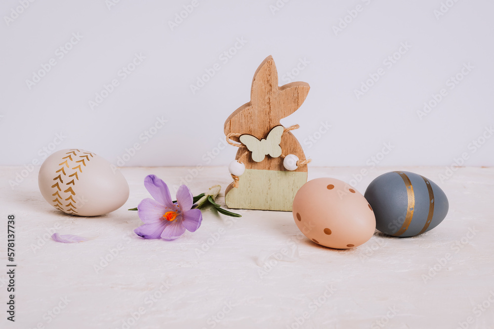 Obraz premium Wooden toy bunny, saffron flower and painted Easter eggs on white table. Easter holiday concept, closeup