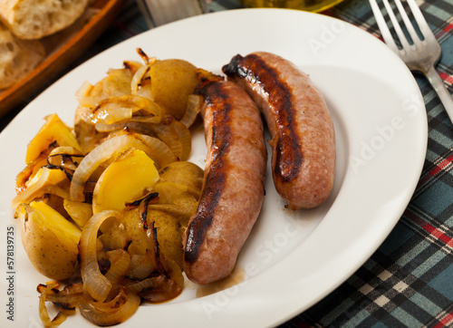 Roasted sausages served with baked potatoes and fried onion on white plate