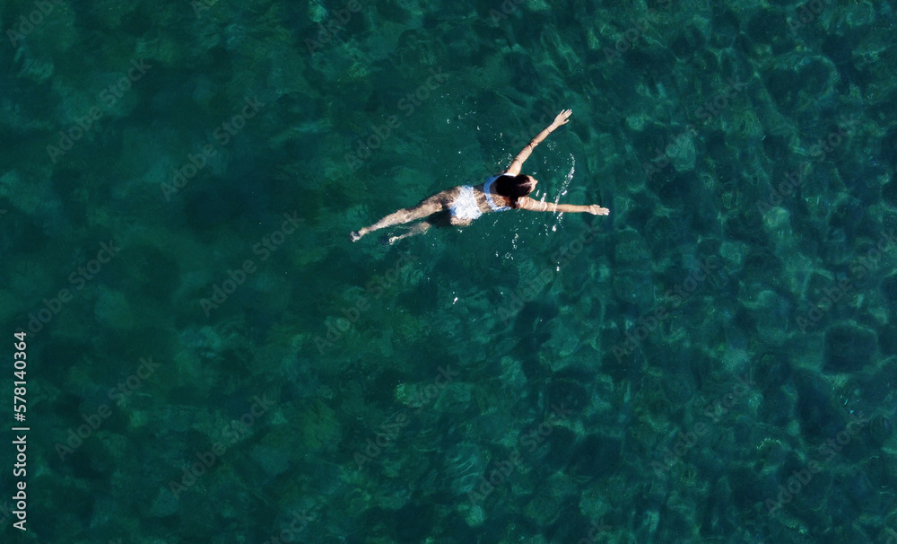 Above view of woman swimming at sea. Aerial top view of young girl in white swimsuit floating on water surface in crystal clear turquoise sea. Vacation at Paradise. Ocean relax, travel and vacation Above view of woman swimming at sea. Aerial top view of young girl in white swimsuit floating on water surface in crystal clear turquoise sea. Vacation at Paradise. Ocean relax, travel and vacation