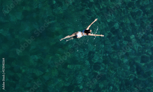 Above view of woman swimming at sea. Aerial top view of young girl in white swimsuit floating on water surface in crystal clear turquoise sea. Vacation at Paradise. Ocean relax, travel and vacation