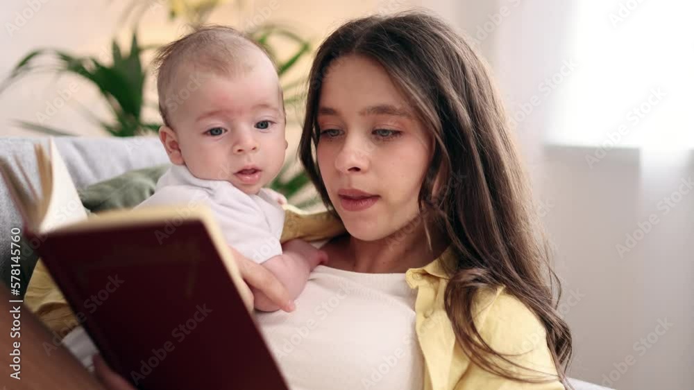 Portrait of cute young family spend leisure time together when mother reading book literature to her little baby soothes the child with his pleasant voice laying on sofa at light room Portrait of cute young family spend leisure time together when mother reading book literature to her little baby soothes the child with his pleasant voice laying on sofa at light room