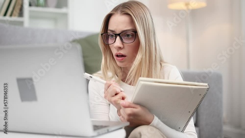 Shocked focused young woman student with glasses listening interesting exciting online lecture with enthusiasm on laptop computer and make notes at home Distance remote education concept