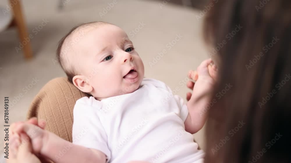 Close up portrait of adorable little baby infant laying on mother legs and enjoying time together at home Mom holding her baby's hand gently and soothes the child with his pleasant voice indoors Close up portrait of adorable little baby infant laying on mother legs and enjoying time together at home Mom holding her baby's hand gently and soothes the child with his pleasant voice indoors