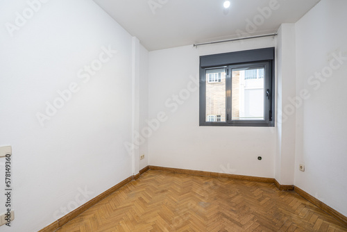 Empty room with herringbone-laid oak parquet flooring, gray aluminum window and white walls © Toyakisfoto.photos