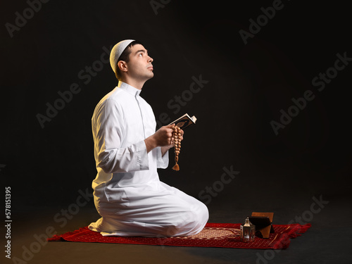 Praying Muslim man with Koran on dark background