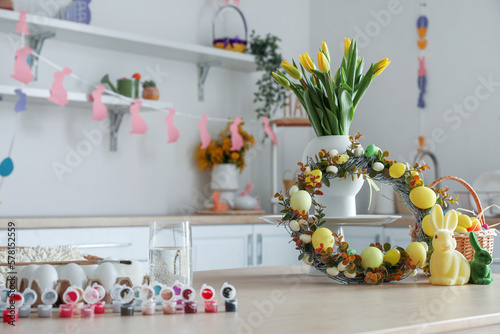 Vase with tulips, Easter wreath, rabbits and basket of eggs on table in kitchen