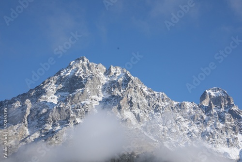 Picturesque landscape of high mountains covered with thick mist under blue sky