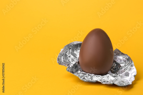 Sticker Tasty chocolate egg with foil on orange background
