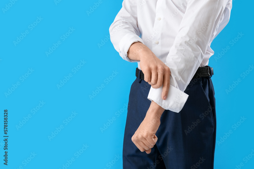 Young businessman rolling up his sleeve on light blue background