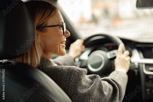Fototapeta Rear view of smiling woman driving car and holding both hands on steering wheel