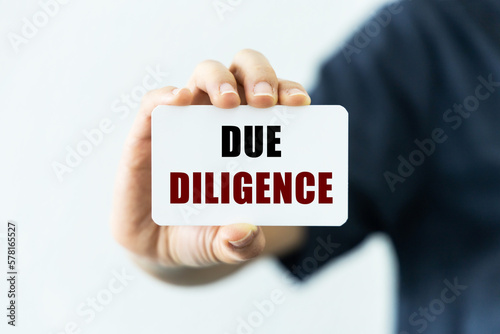 Due diligence text on blank business card being held by a woman's hand with blurred background. Business concept about due diligence.