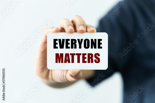 Everyone matter text on blank business card being held by a woman's hand with blurred background. Business concept about everyone matter. photo