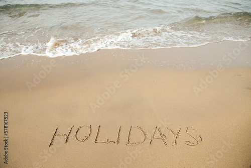 Holidays lettering on the beach with wave and clear blue sea. 