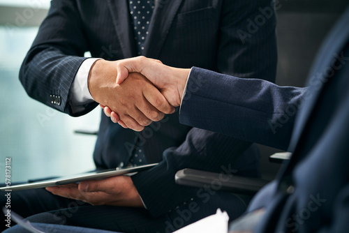 two asian businessmen sitting in chair shaking hands in office