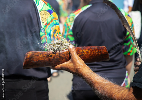 Human hand hold wooden dish with branches against background of traditional ornament, the smoke ritual rite at a indigenous community event in Australia 