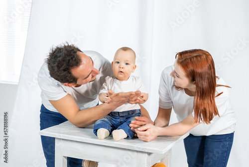 young parents lovingly look, play, kiss the child. white interior