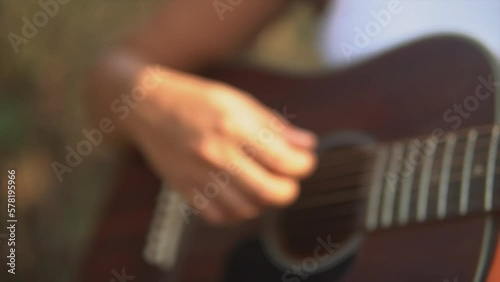 Close up push out shot in slow motion of a female hand strumming the guitar during sunset. 