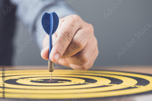 Businessman working in the office and throwing arrow darts in the center of yellow dartboard. Goal and success for business concept.