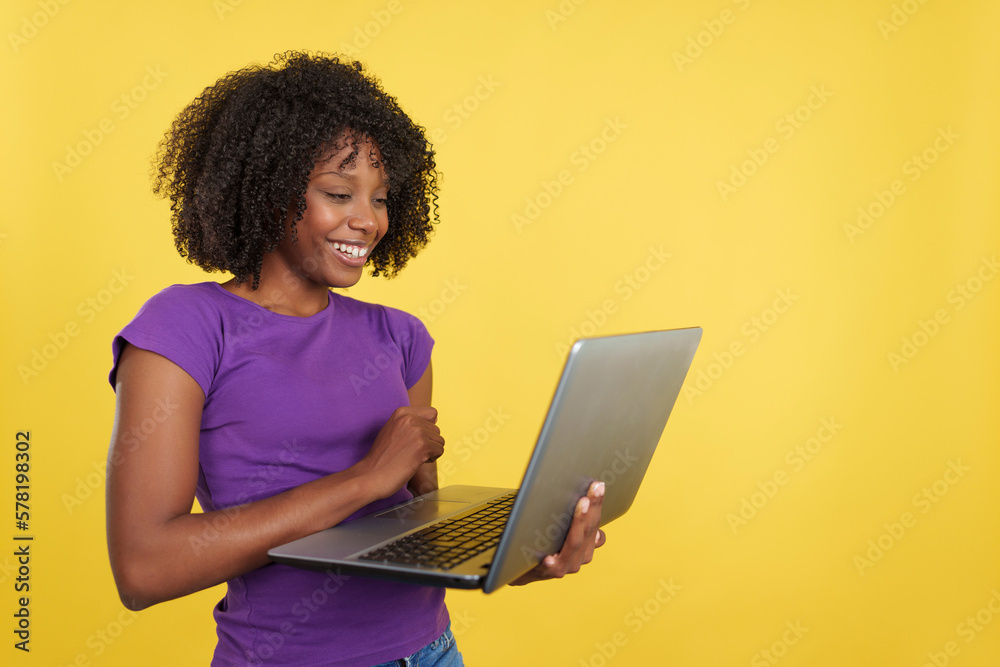 Woman with afro hairstyle smiling while using a laptop Woman with afro hairstyle smiling while using a laptop