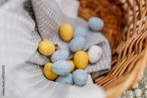 Blue, yellow, white eggs and white small flowers lie in a basket close-up. Spring Background for Easter