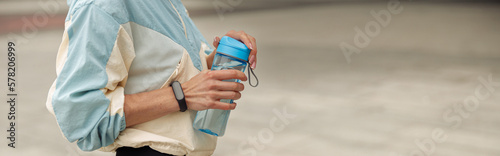CLose up of sportive woman stands with bottle of water after running in city. Healthy lifestyle