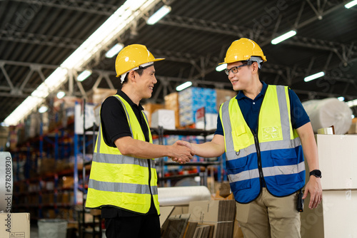 Asian warehouse workers team shaking hands together in the storage warehouse, feeling happy and smiling. teamwork at warehouse storage department.