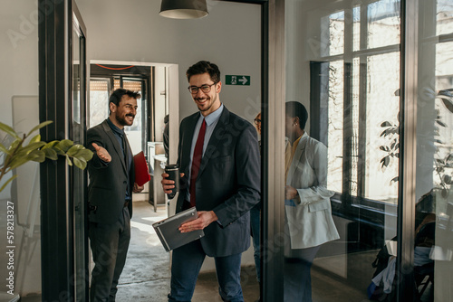 Shot of a group of a businessman holding the door while his coworkers enter the office. Confident young business people working together in the office. photo