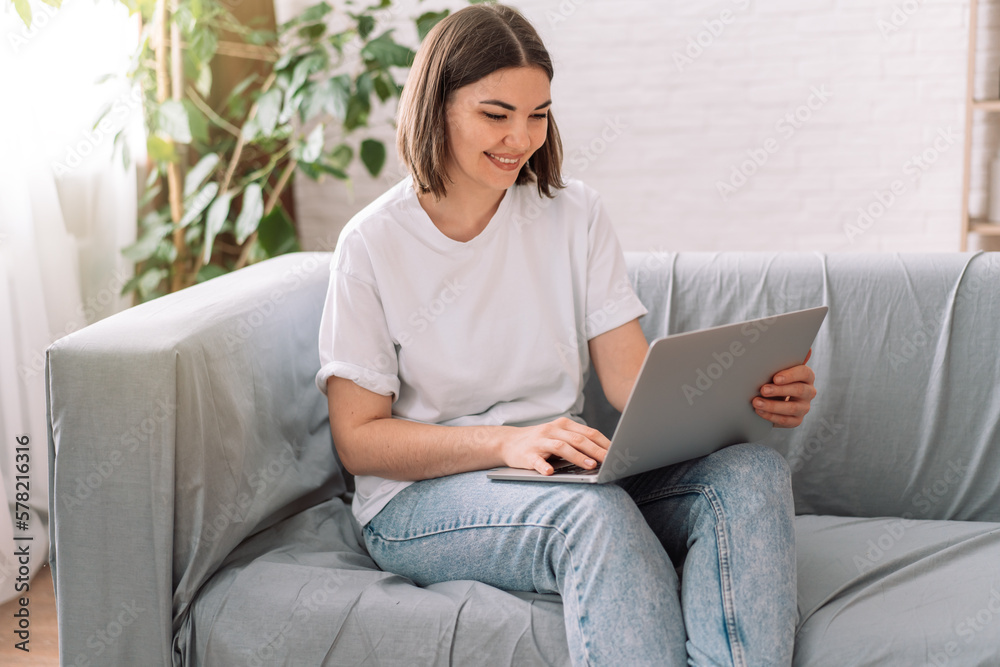 Naklejka premium Lady sitting on gray sofa reading with laptop.