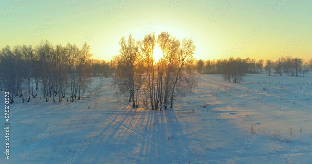 Aerial drone view of cold winter landscape with arctic field, trees covered with frost snow and morning sun rays over horizon. Extreme weather. Aerial drone view of cold winter landscape with arctic field, trees covered with frost snow and morning sun rays over horizon. Extreme weather.