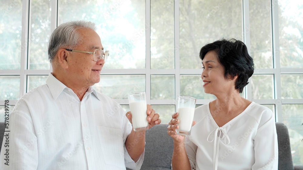 Happy Asian elderly couple relaxing and drinking milk on the sofa at home. Happy senior retirement lifestyle Happy Asian elderly couple relaxing and drinking milk on the sofa at home. Happy senior retirement lifestyle