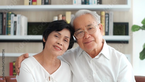 Asian elderly couple. Joyful nice elderly couple smiling looking at camera while being in a great mood, smiling healthy senior retired grandparents husband and wife happy faces embracing at home © M Stocker