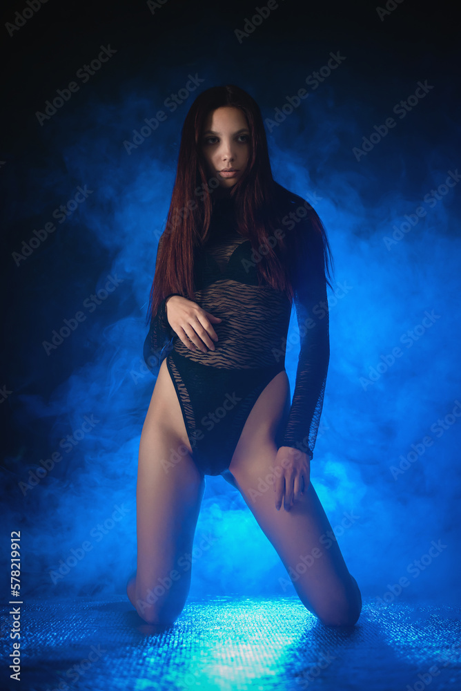 Beautiful girl a dancer in the black body suit on the dark background in the blue lights.
