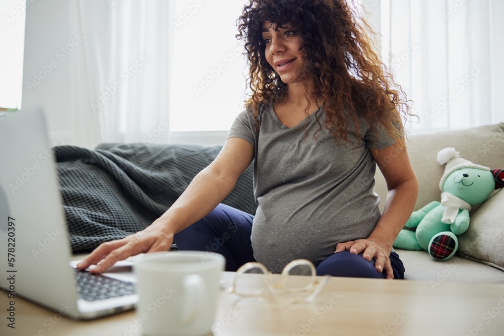 A pregnant woman sits on the sofa at home and orders goods for pregnant women on the Internet, online shopping. Home clothes, lifestyle of a pregnant woman, preparation for childbirth A pregnant woman sits on the sofa at home and orders goods for pregnant women on the Internet, online shopping. Home clothes, lifestyle of a pregnant woman, preparation for childbirth