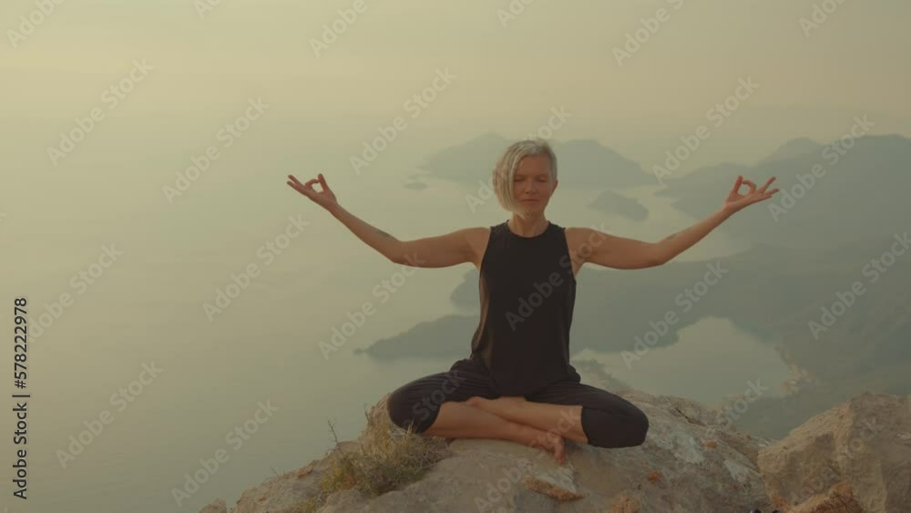 Concept of yoga and tranquility. Meditation and yoga practice on top of the mountain. Young woman sits lotus position on top of rock Concept of yoga and tranquility. Meditation and yoga practice on top of the mountain. Young woman sits lotus position on top of rock