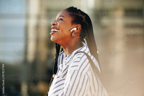 Sideview of a cheerful young businesswoman listening to music on her way to work in the city