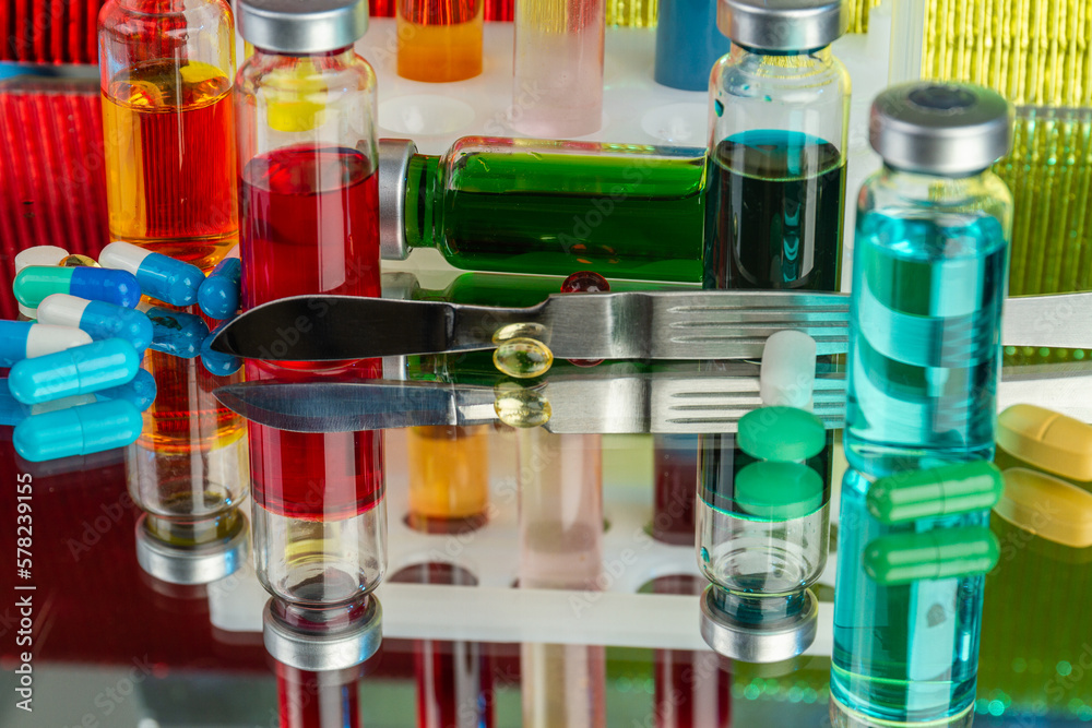Close up colored drug vials with medicine solution. Lab drugs on reflective surface. Close up colored drug vials with medicine solution. Lab drugs on reflective surface.