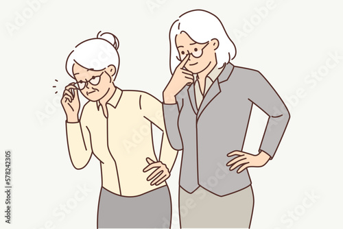Two elderly women in business clothes carefully look to side watching work of young employees