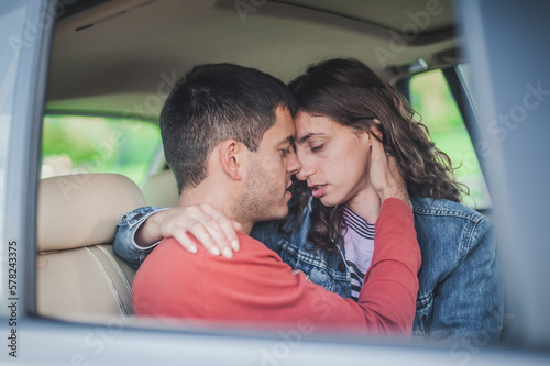 Passionate kiss in car. View through the window. Young sexy couple in love, sitting in the back seat, looking and kissing passionately each other, just before sex. Desire, passion and love concept