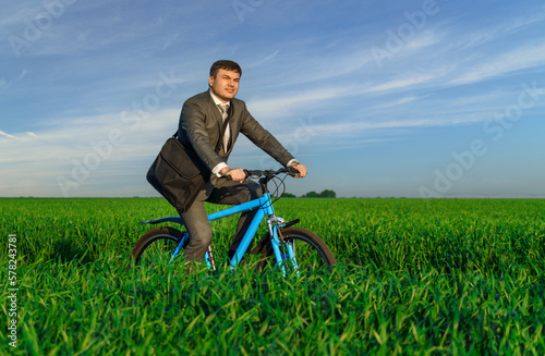 a businessman rides a bicycle on a green grassy field, dressed in a business suit, beautiful nature in spring, freelance business concept