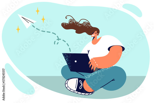 Woman sits on floor with laptop on lap working as copywriter writing mailing letters