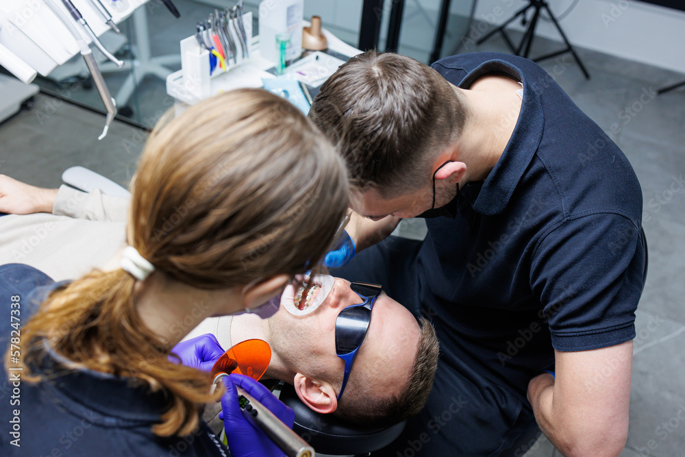 An orthodontist with an assistant treats teeth using dental instruments. Dental office. Orthodontic treatment of teeth An orthodontist with an assistant treats teeth using dental instruments. Dental office. Orthodontic treatment of teeth