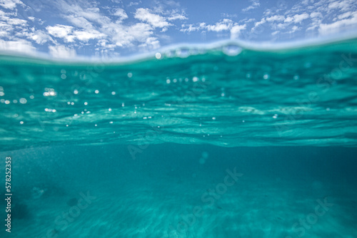 A split level shot of turquoise ocean water and clouds in a blue sky