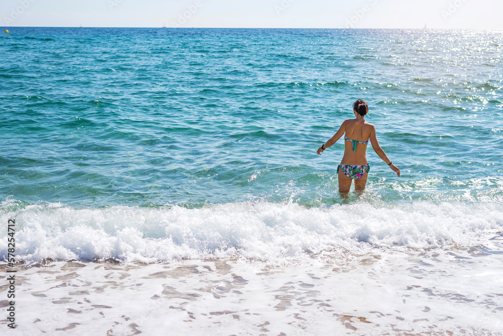 Rear view of young beautiful woman taking a bath at beach in daylight Rear view of young beautiful woman taking a bath at beach in daylight