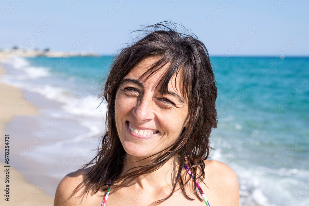 Beautiful woman standing on beach while smiling against blue sky Beautiful woman standing on beach while smiling against blue sky