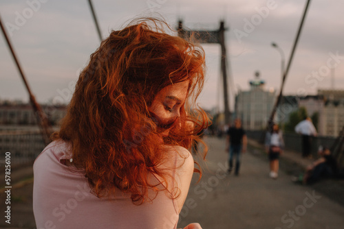 Back view of woman with red hair walking on bridge in city photo
