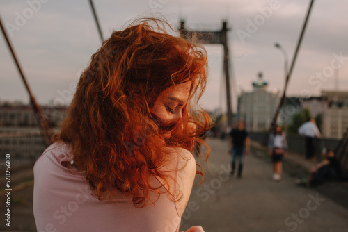 Back view of woman with red hair walking on bridge in city