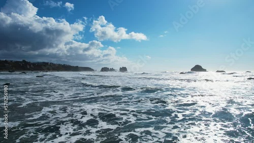 Stunning 4K aerial drone shot gliding over blue ocean waves in Bandon, Oregon with vibrant blue clouds. photo