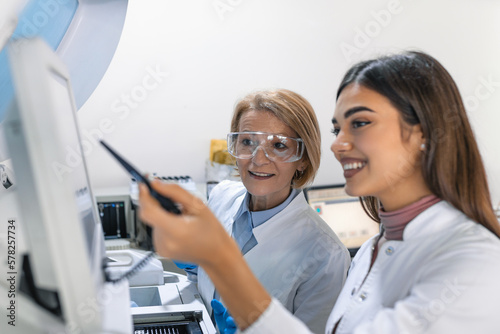 Two Research Scientists Programm Medical Equipment with Tablet Computer. Team of Professionals Doing Pharmaceutical Research in Modern Laboratory.